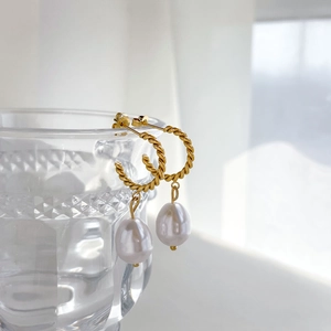 Détail de boucles d'oreilles créoles torsadées dorées avec perles baroques sur verre