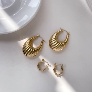 Detail of golden croissant hoop earrings and beaded small rings on a grey background