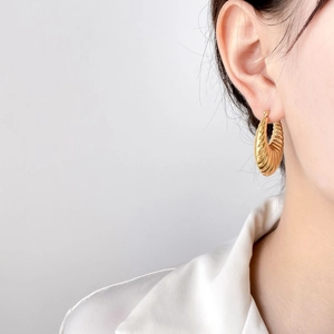 Detail of gold ribbed oval hoop earrings on model featuring elegant textured metal design