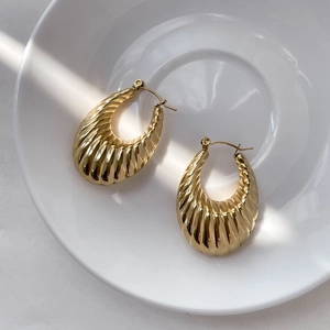 Detailed view of thick gold hoop earrings with vertical ribbed texture on white ceramic plate