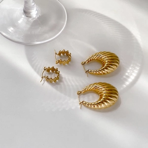 Detail of gold beaded hoop and ribbed croissant earrings on a white elegant background