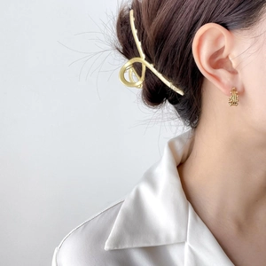 Detail view of a model wearing a gold minimalist hair clip and textured bead earrings