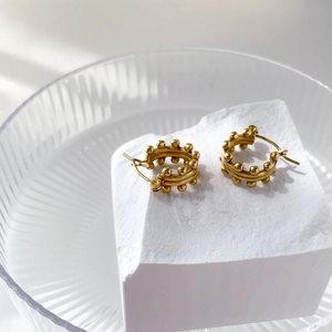 Macro detail of gold beaded hoop earrings resting on white stone and glass textures