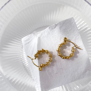 Detail shot of golden hoop earrings with beaded texture on a white stone background