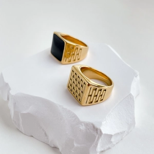 Modern gold rings featuring square black face and embossed texture on a stone stand