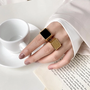Macro detail of gold grid texture ring and square black enamel ring on model hand