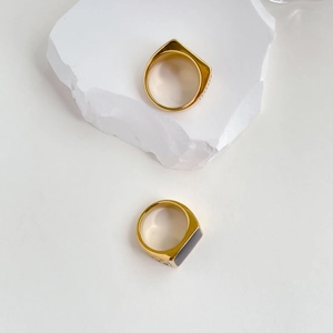 Close-up of golden square signet rings with black inlay on a white stone background