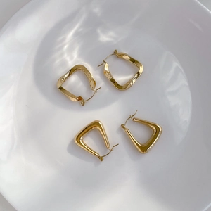 Detail of minimalist geometric gold stud earrings on a white aesthetic background