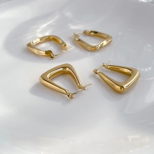 Detailed shot of gold-plated geometric U-shaped and rectangular earrings on a ceramic tray