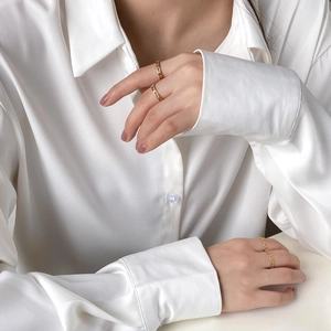 Gros plan de bagues dorées à maillons portées avec une chemise en soie blanche chic