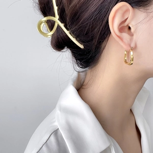 Close-up of a model wearing gold U-shaped earrings and a minimalist metal hair claw clip