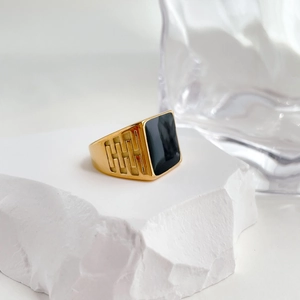 Detailed view of gold signet ring with black enamel top on textured white stone