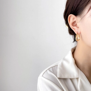 Close-up of minimalist gold rectangular hoop earrings worn by a model in a modern style