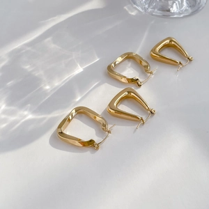 Macro detail of two pairs of minimalist gold geometric hoop earrings with light water reflections