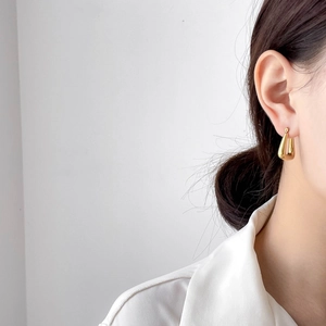 Close-up of polished gold teardrop earrings worn by a model in a minimalist style