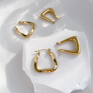 Detailed view of gold geometric hoop earrings on a stone surface with water ripple shadows