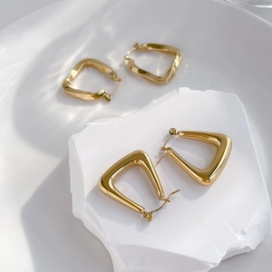 Detailed macro view of gold geometric triangle earrings on minimalist white pedestal