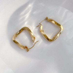 Detailed view of gold twisted square hoop earrings on a rippling water background