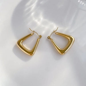 Macro shot of 18K gold geometric triangular hoop earrings on a minimalist white backdrop