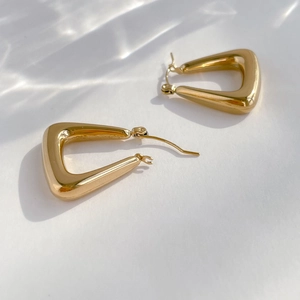 Macro view of geometric triangular hoop earrings with polished gold mirror finish