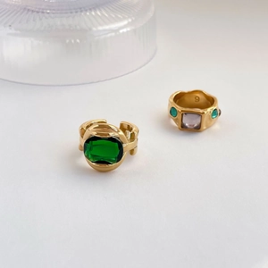 Macro view of vintage gold rings with emerald and purple stones on a beige background
