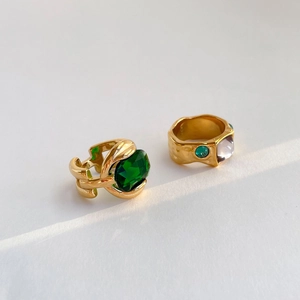 Detailed macro view of gold-plated rings with emerald and white gemstones on white paper
