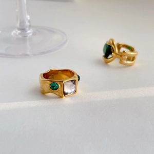 Luxurious gold rings set with square white stones and emerald green gems on white surface