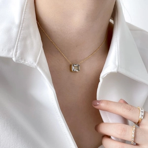 Detail of square zircon pendant necklace and gold rings worn with white shirt