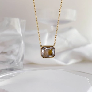 Minimalist gold necklace with a square gray zircon pendant on white silk fabric