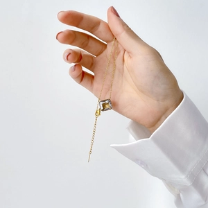 Detailed view of square zircon pendant on a gold chain held against white shirt