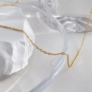 Close-up of a delicate golden zircon necklace chain draped over textured white stone