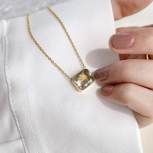 Close-up of rectangular zircon pendant on a gold necklace held by hand against white fabric