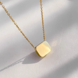 Detailed close-up of a minimalist gold square pendant on a fine link chain with soft lighting