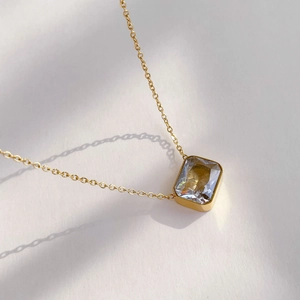 Detail of square zircon pendant on gold chain with matte finish and multifaceted cut