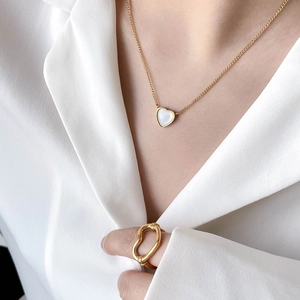 Detail of elegant gold heart necklace with shell pendant and matching thin gold ring