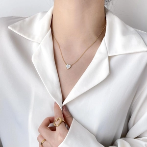 Golden heart necklace with white pearl inlay worn by a model in a satin shirt