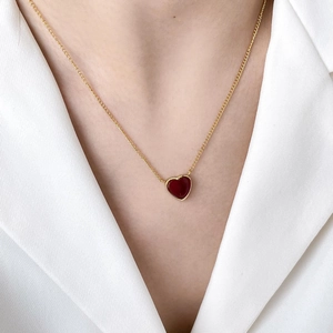 Close-up of a delicate gold heart necklace with a red pendant on a woman's neck