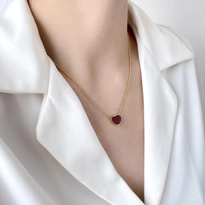 Close-up of a small red heart pendant necklace on a woman wearing a white V-neck shirt