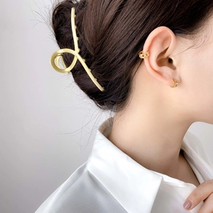 Detail showing a golden chain ear cuff and studded hoop earrings on a female model
