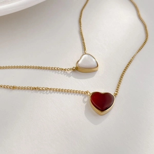 Detail of gold heart necklaces featuring red agate and white mother of pearl pendants