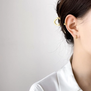 Close-up of golden chain ear cuff and star stud earrings worn by a model