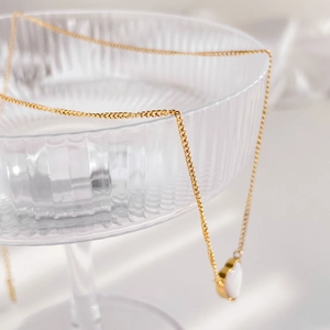 Close-up of golden necklace with a white heart pendant on textured glass base