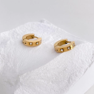 Macro detail of gold-plated starburst huggie earrings with white cubic zirconia stones