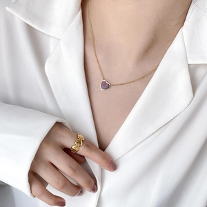 Close-up of a gold heart necklace with purple stone and matching ring on a white shirt