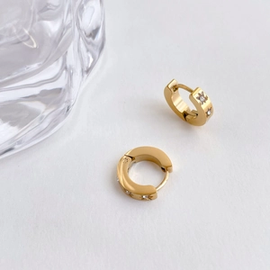 Detail of gold huggie earrings with star-set crystals and minimalist glass background