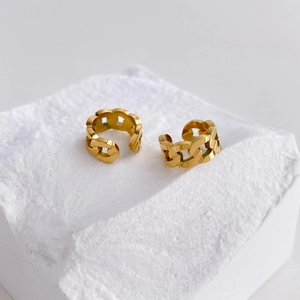 Detail shot of golden Cuban chain link cuff earrings on a textured stone display