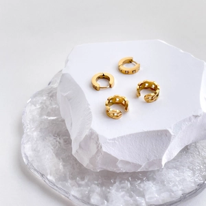 Close-up of gold chain ear cuffs and star engraved hoop earrings on white stones