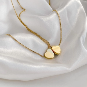 Detailed view of two gold heart necklaces on a luxurious white silk fabric backdrop