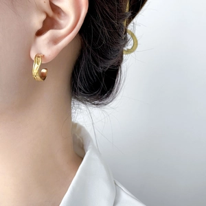 Close-up of golden triple-layered C-shaped earrings with a polished twisted design on model