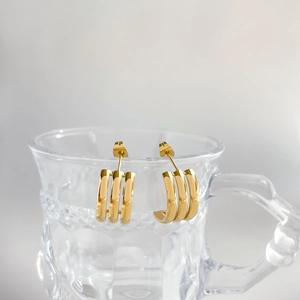 Minimalist gold triple-band C-shaped hoop earrings hanging on a glass rim closeup